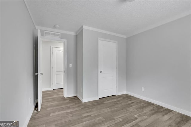 unfurnished bedroom featuring wood finished floors, a textured ceiling, baseboards, and ornamental molding