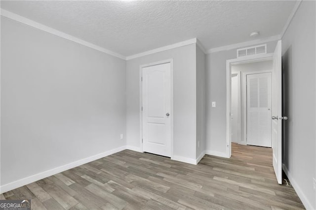 unfurnished bedroom with wood finished floors, a textured ceiling, baseboards, and ornamental molding