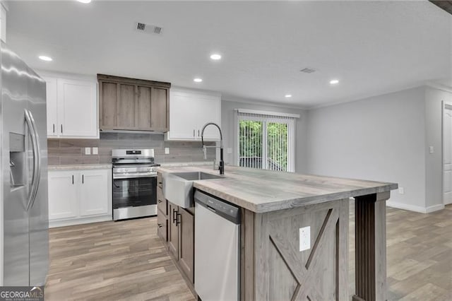 kitchen featuring stainless steel appliances, a sink, light wood-type flooring, light countertops, and an island with sink