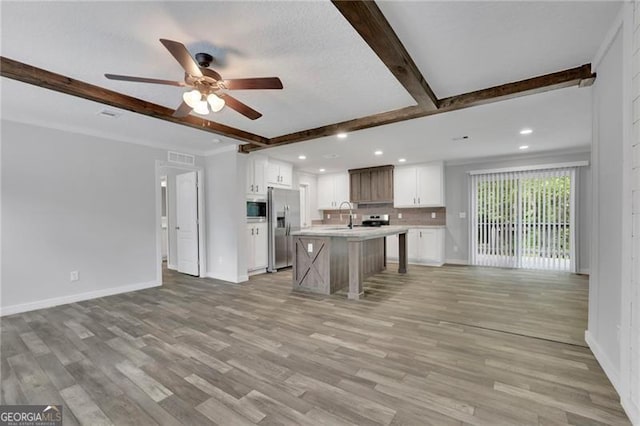 kitchen featuring stainless steel fridge with ice dispenser, open floor plan, beamed ceiling, a sink, and built in microwave