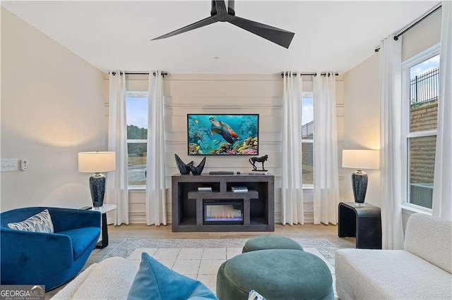 tiled living area featuring a ceiling fan and a glass covered fireplace