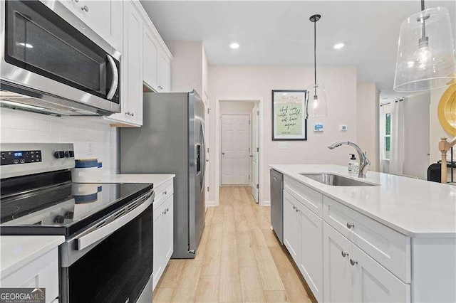 kitchen featuring stainless steel appliances, a sink, white cabinetry, light countertops, and decorative light fixtures