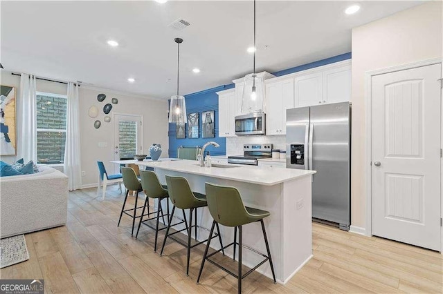 kitchen with stainless steel appliances, a center island with sink, a kitchen bar, light wood-style flooring, and a sink
