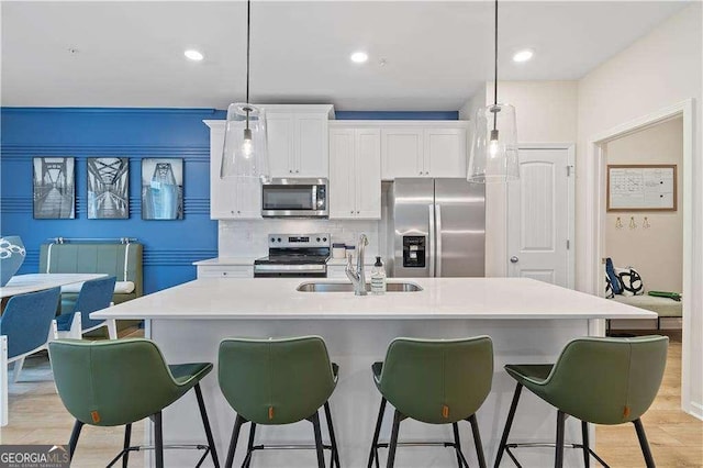 kitchen featuring stainless steel appliances, a sink, a kitchen bar, white cabinetry, and pendant lighting
