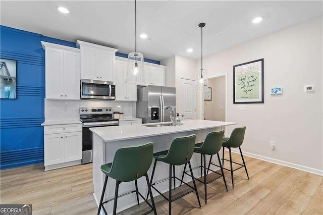 kitchen featuring appliances with stainless steel finishes, a sink, an island with sink, light countertops, and white cabinets