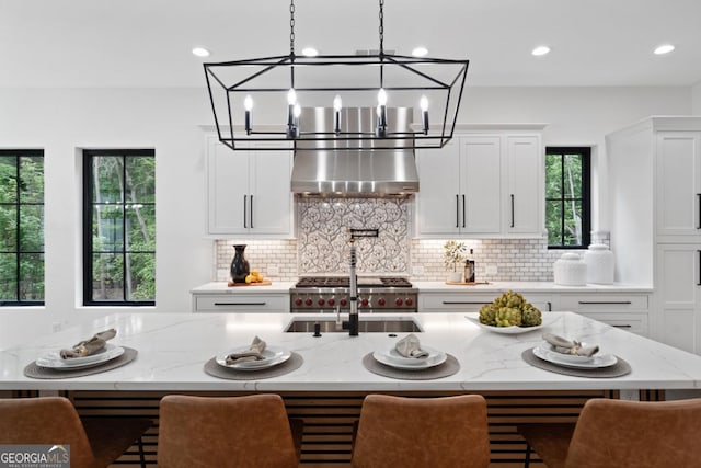 2595 Grassview Dr, Milton, GA 30004 - kitchen featuring wall chimney exhaust hood, a chandelier, decorative backsplash, light stone countertops, and white cabinets