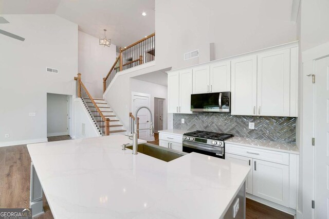 8370 Pleasant Grove Cir, Gainesville, GA 30506 - kitchen with appliances with stainless steel finishes, a high ceiling, backsplash, an island with sink, and white cabinetry
