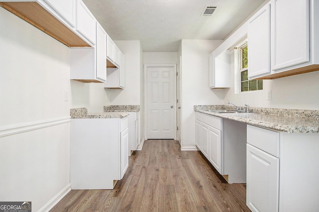 kitchen with a sink, wood finished floors, white cabinetry, baseboards, and light stone counters