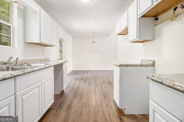 kitchen featuring wood finished floors, a sink, white cabinets, and baseboards