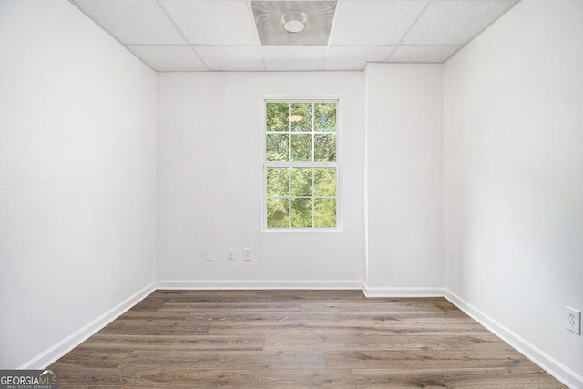 empty room featuring a paneled ceiling, wood finished floors, and baseboards