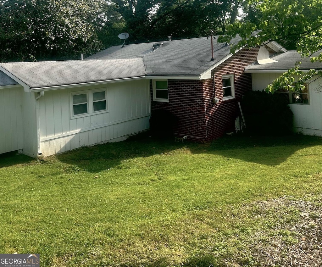 back of house featuring a lawn and roof with shingles