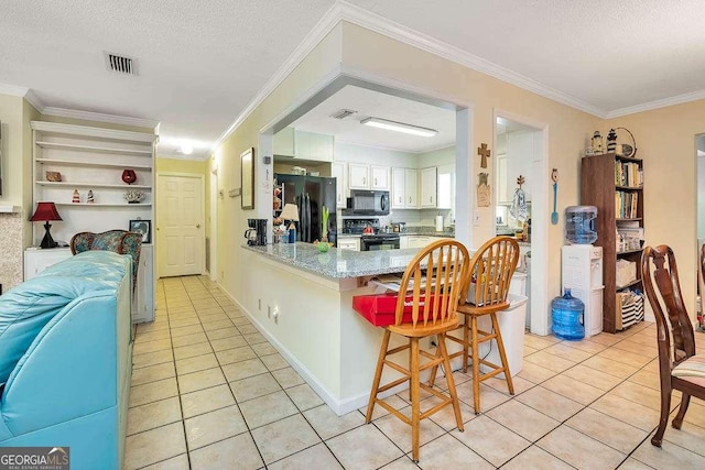 503 Marsh Cir, Saint Simons, GA 31522 - kitchen with black appliances, light tile patterned floors, a peninsula, a breakfast bar area, and a textured ceiling