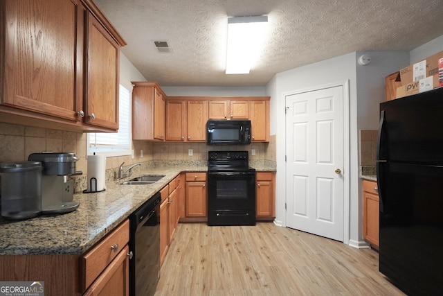 kitchen with black appliances, light wood finished floors, a sink, backsplash, and a textured ceiling