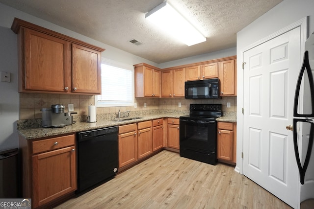 kitchen featuring black appliances, a sink, light wood-style flooring, tasteful backsplash, and a textured ceiling