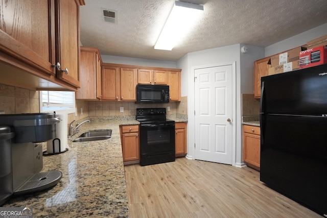 kitchen with black appliances, a sink, decorative backsplash, light wood-type flooring, and light stone counters