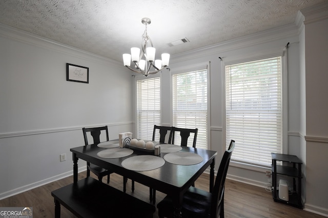 dining area with a chandelier, wood finished floors, ornamental molding, a textured ceiling, and baseboards