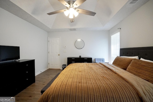 bedroom with dark wood finished floors, baseboards, lofted ceiling, ceiling fan, and a tray ceiling