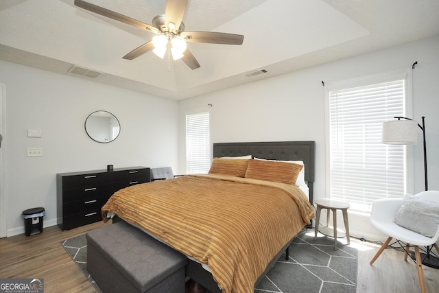 bedroom featuring a tray ceiling, baseboards, wood finished floors, and a ceiling fan
