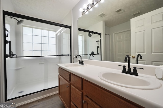 full bath with a stall shower, a textured ceiling, double vanity, and wood finished floors