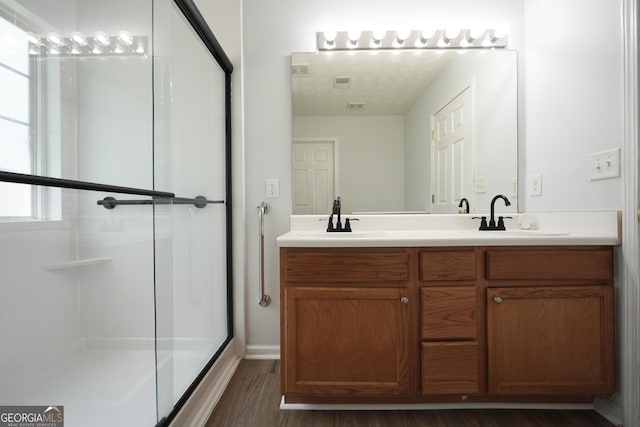 bathroom with a shower with door, wood finished floors, and double vanity