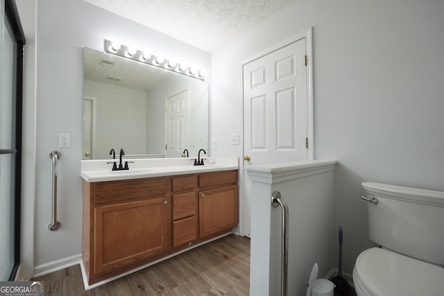 bathroom with wood finished floors, toilet, double vanity, and a textured ceiling