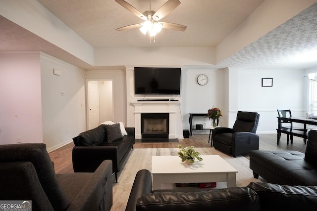 living room with light wood finished floors, a ceiling fan, a fireplace with flush hearth, and baseboards