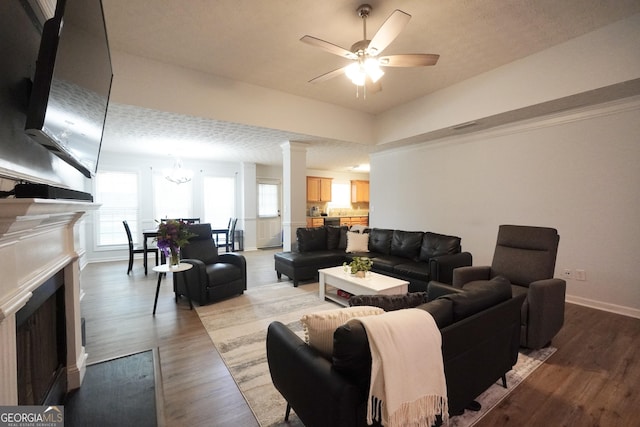 living room featuring a fireplace with flush hearth, wood finished floors, a ceiling fan, baseboards, and a chandelier