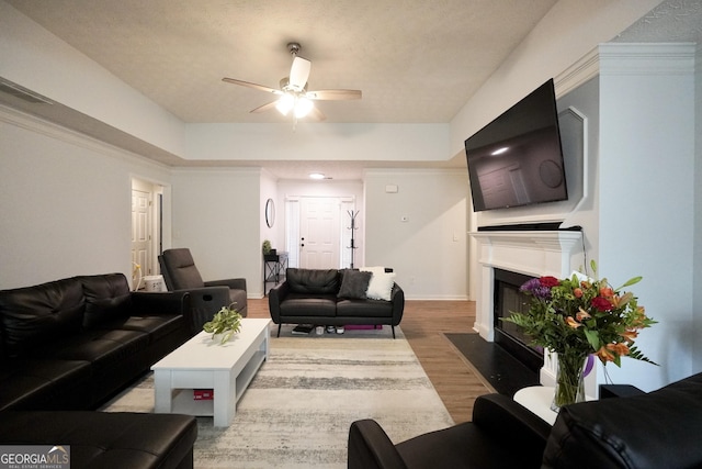 living area featuring a fireplace with flush hearth, ceiling fan, wood finished floors, baseboards, and a textured ceiling