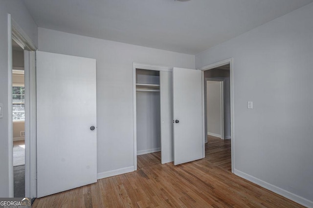 unfurnished bedroom featuring wood finished floors, baseboards, and a closet
