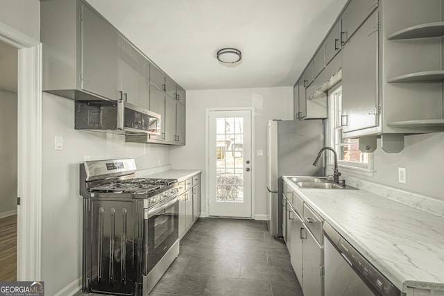 kitchen featuring stainless steel appliances, open shelves, gray cabinets, and baseboards