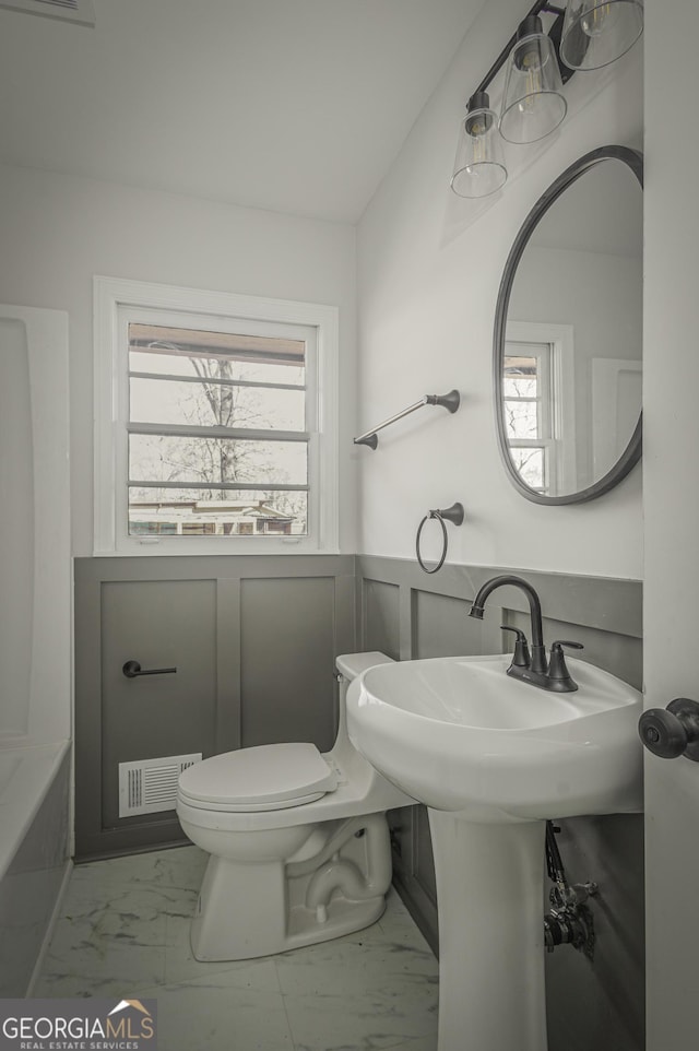 bathroom with marble finish floors, wainscoting, toilet, and a tub to relax in