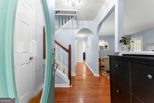 foyer with light wood finished floors, arched walkways, stairs, baseboards, and a textured ceiling