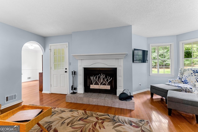 living area featuring hardwood / wood-style floors, arched walkways, baseboards, a textured ceiling, and a premium fireplace