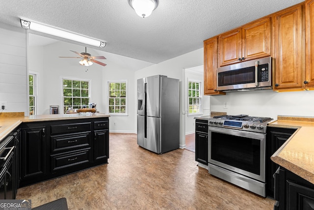 kitchen with stainless steel appliances, vaulted ceiling, light countertops, a ceiling fan, and a textured ceiling