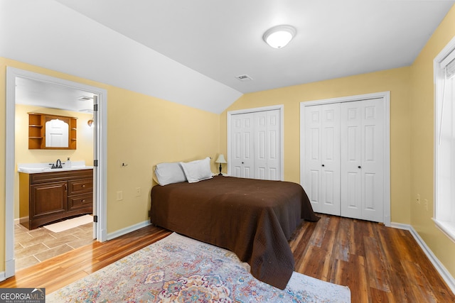 bedroom with wood finished floors, multiple closets, baseboards, lofted ceiling, and a sink
