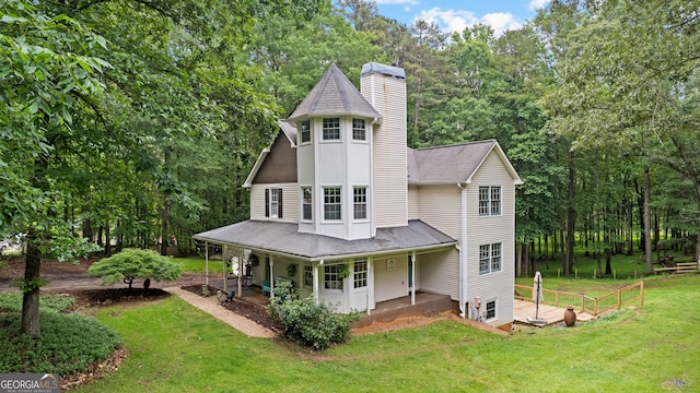 back of property featuring a chimney, a yard, a porch, a shingled roof, and view of scattered trees