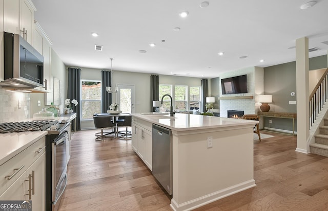 4297 Azalea Ridge Way, Hoschton, GA 30548 - kitchen with appliances with stainless steel finishes, a sink, tasteful backsplash, a fireplace, and light wood finished floors