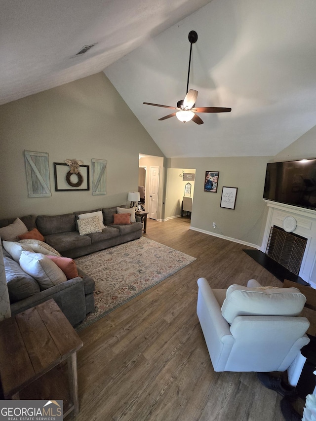 living area featuring lofted ceiling, a fireplace, ceiling fan, wood finished floors, and baseboards
