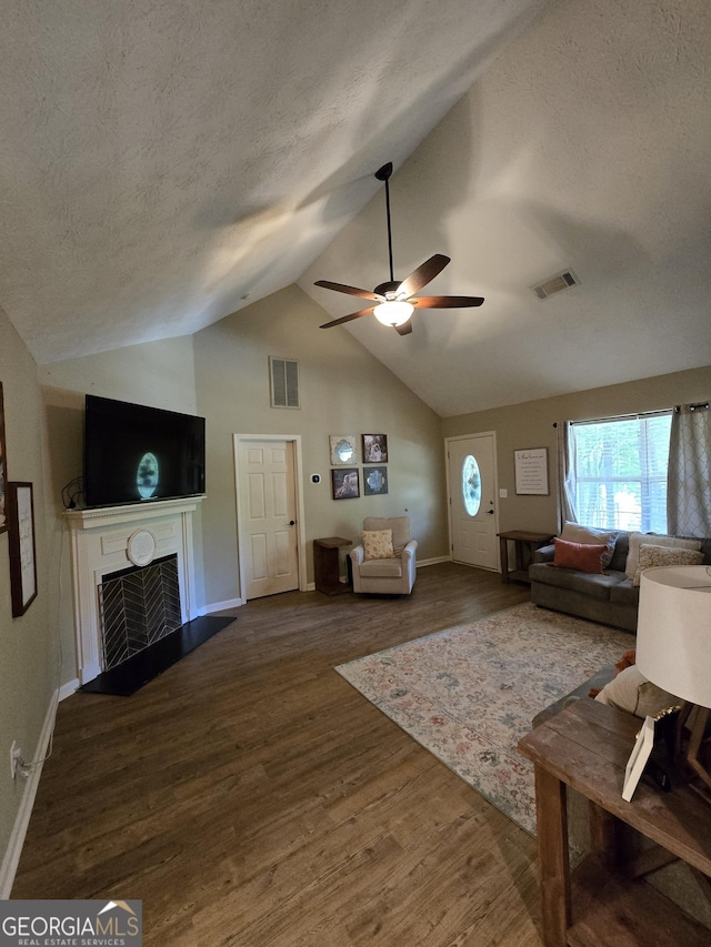 living area featuring a fireplace with flush hearth, vaulted ceiling, ceiling fan, wood finished floors, and a textured ceiling