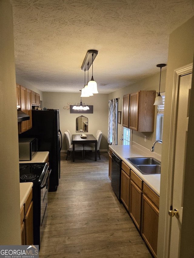 kitchen with a sink, black appliances, light countertops, hanging light fixtures, and a textured ceiling