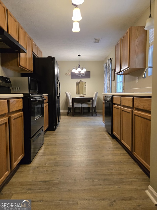 kitchen with black appliances, extractor fan, brown cabinets, and hanging light fixtures