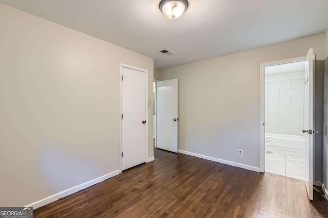 unfurnished bedroom featuring wood-type flooring, baseboards, and connected bathroom