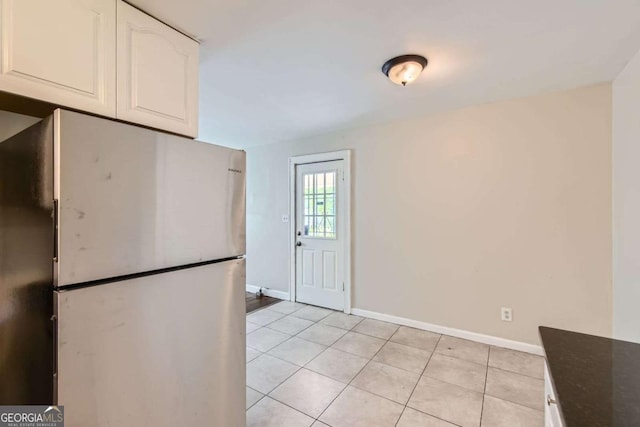 kitchen with freestanding refrigerator, white cabinetry, baseboards, light tile patterned floors, and dark stone counters