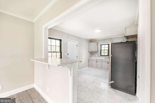 kitchen featuring freestanding refrigerator, crown molding, light marble finish flooring, a breakfast bar, and light countertops