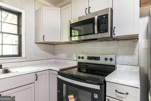 kitchen with appliances with stainless steel finishes, backsplash, light countertops, and ornamental molding