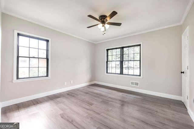 empty room featuring healthy amount of natural light, ornamental molding, ceiling fan, and wood finished floors