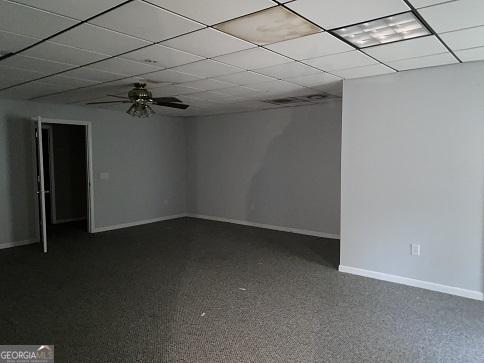 spare room with dark carpet, a ceiling fan, baseboards, and a drop ceiling