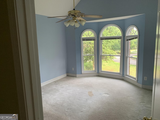 carpeted empty room with lofted ceiling, baseboards, and a ceiling fan