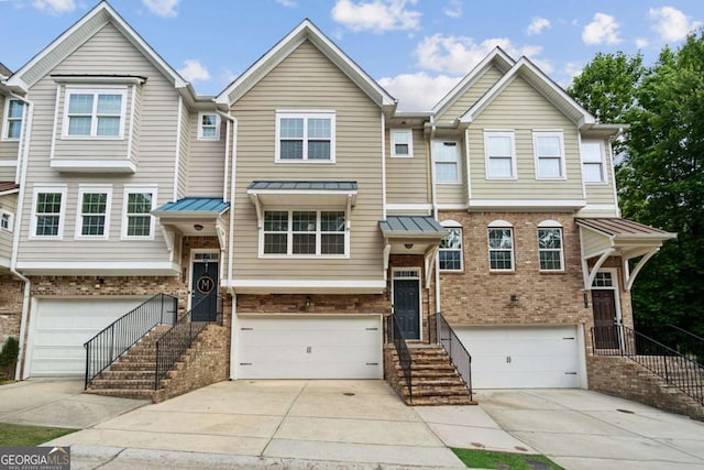 townhome / multi-family property featuring an attached garage, driveway, a standing seam roof, and brick siding