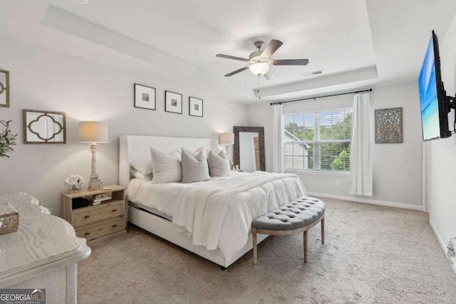 bedroom with light carpet, a tray ceiling, baseboards, and a ceiling fan